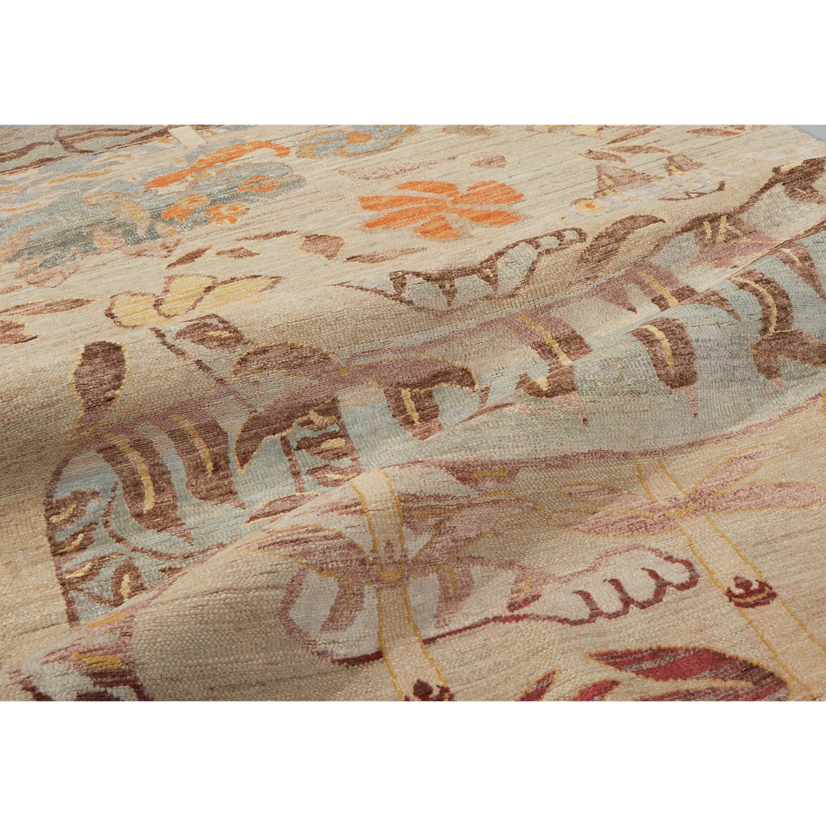 A close-up of a woven textile or rug with a muted floral and abstract pattern in beige, brown, pale blue, orange, and burgundy tones.