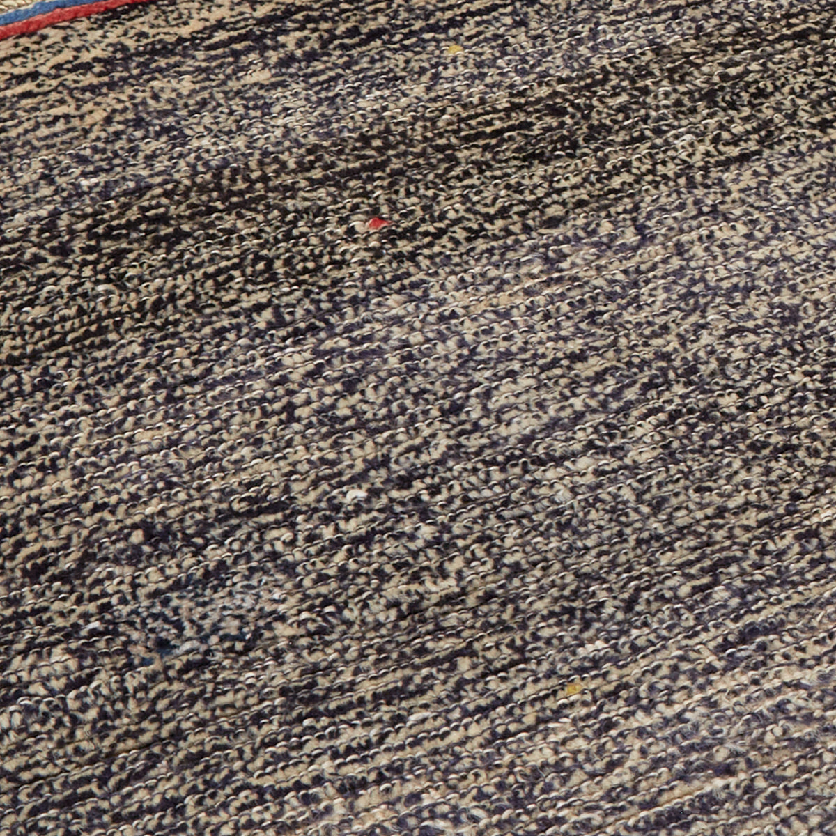 A close-up of a textured rug or carpet with a dense, mottled pattern of black, beige, and brown tones.