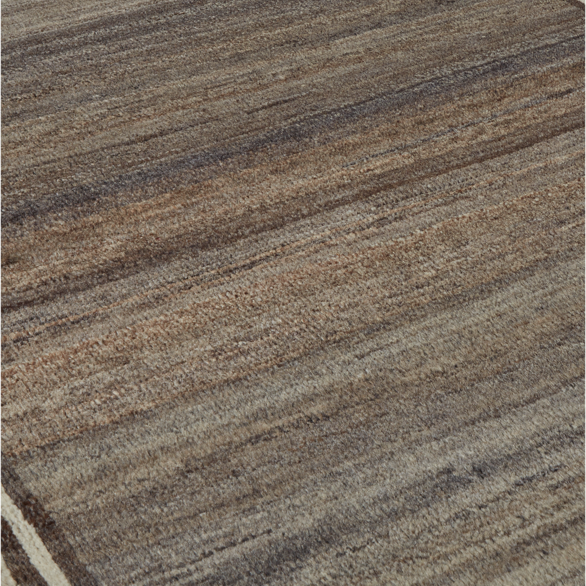 A close-up of a textured area rug with a rustic, hand-woven appearance. The color palette consists of blended earthy tones including brown, beige, gray, and muted blue-gray, arranged in diagonal horizontal stripes.
