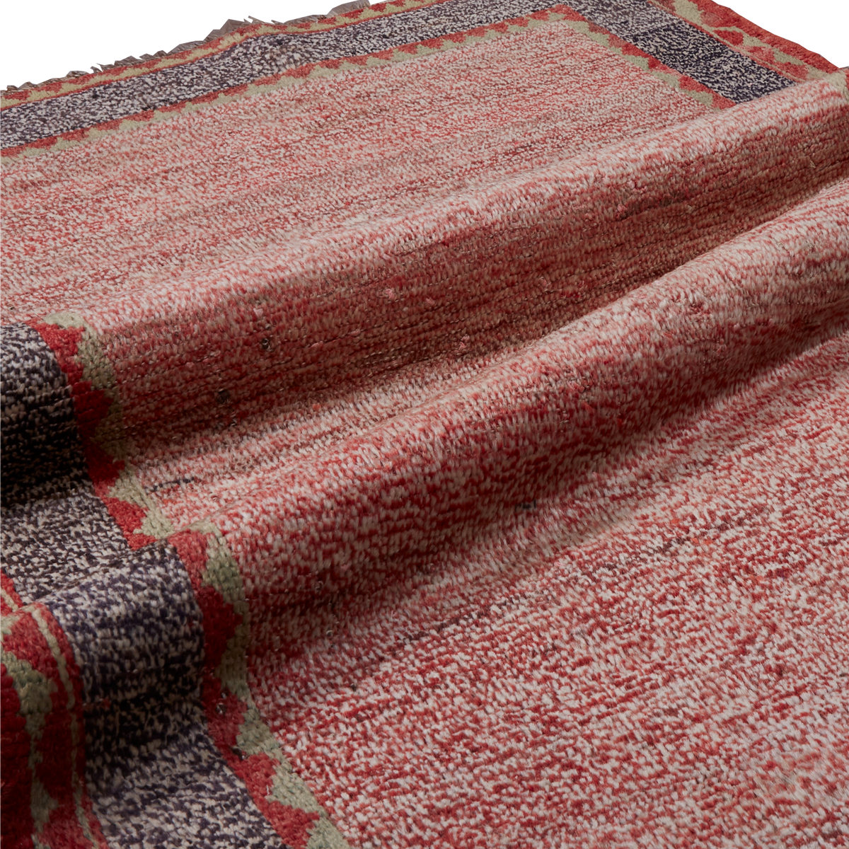 A close-up of a textured woven textile, likely a rug or blanket, featuring a mottled red and cream pattern with a dark gray and red geometric border.