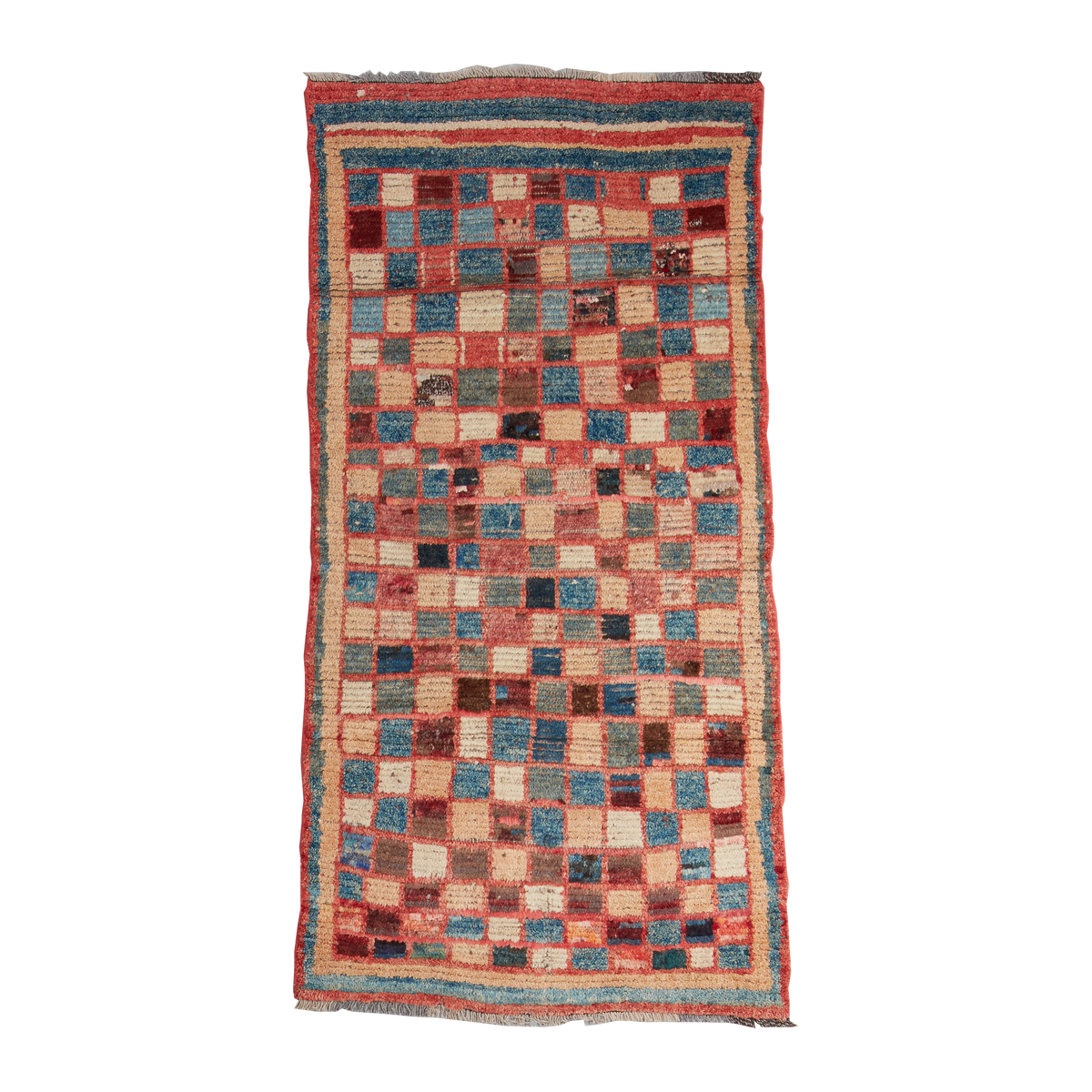 A rectangular patchwork rug with a checkerboard pattern in muted red, blue, beige, and brown tones, featuring a striped border and fringed edges, shown flat against a white background.
