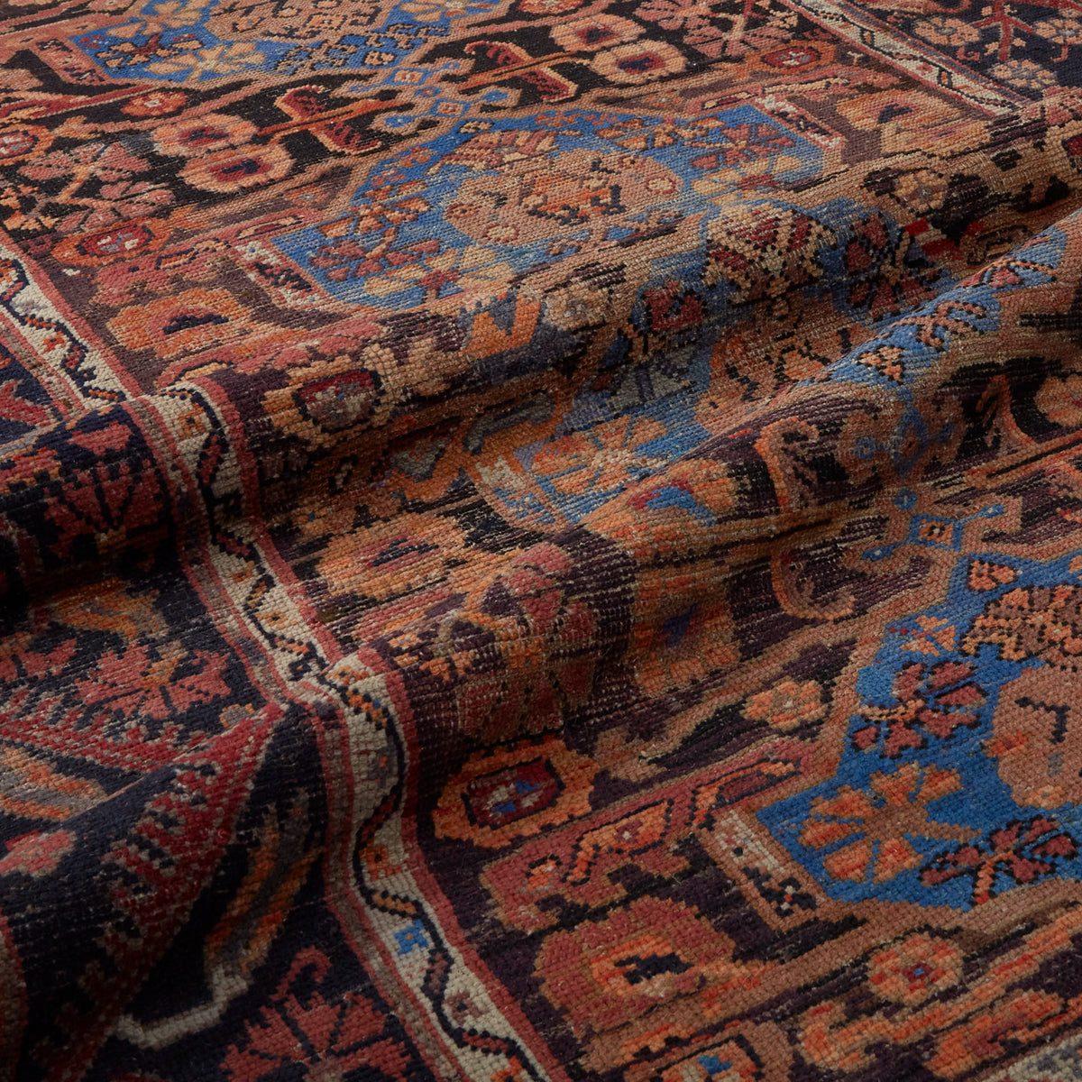A close-up of a folded vintage-style Persian rug with a complex floral and geometric pattern in dark brown, rust red, blue, and cream.