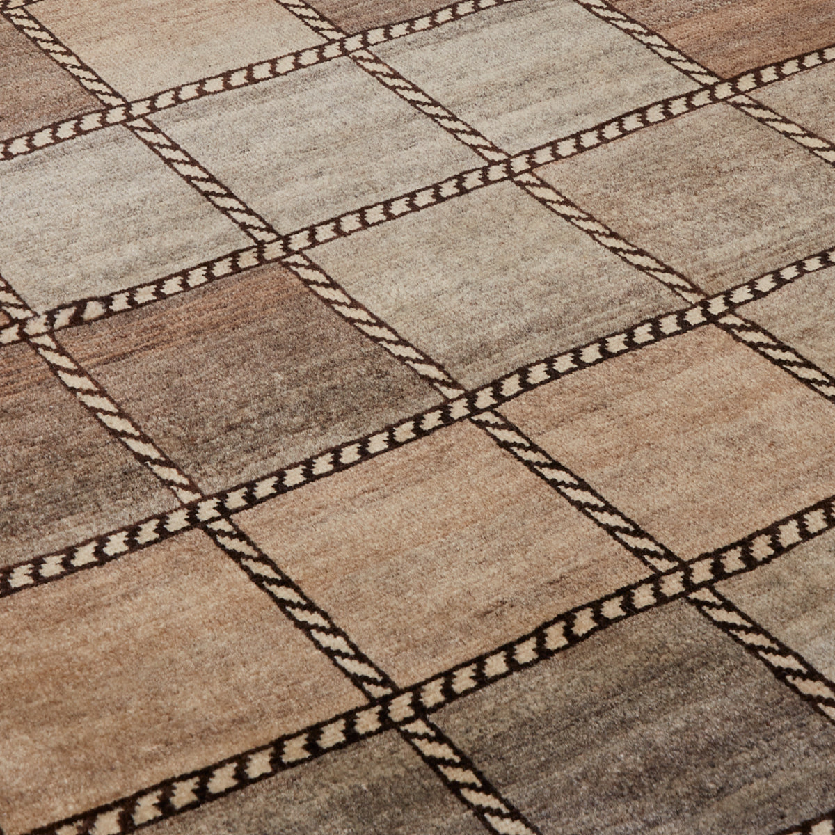A close-up of a woven rug with a geometric diamond pattern in shades of beige, brown, and gray, separated by dark brown rope-like lines.