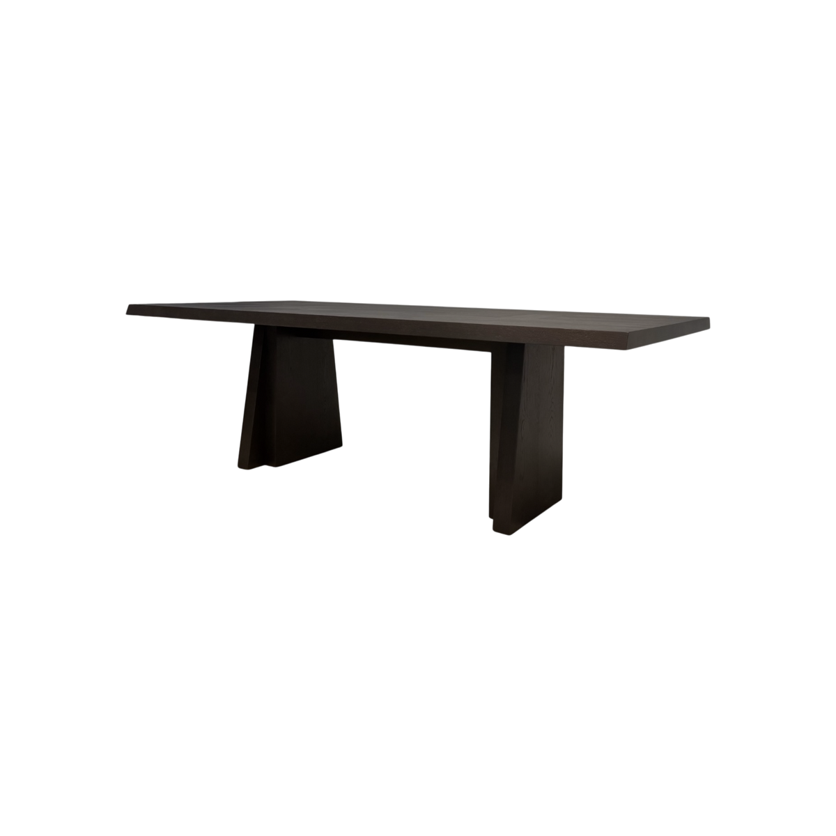 Angled view of the Oblique 96-inch Dining Table showing its elongated dark wood top, chamfered edges and sculptural splayed pedestal bases.