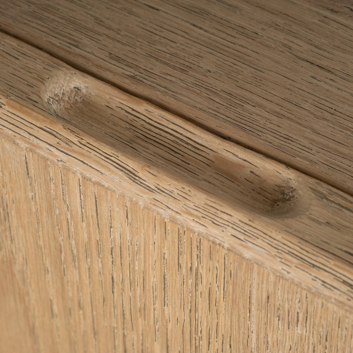 Close-up showing the carved pull on the Rosedale Cabinet’s top edge in light tan oak, with open grain and a pale limewashed finish.