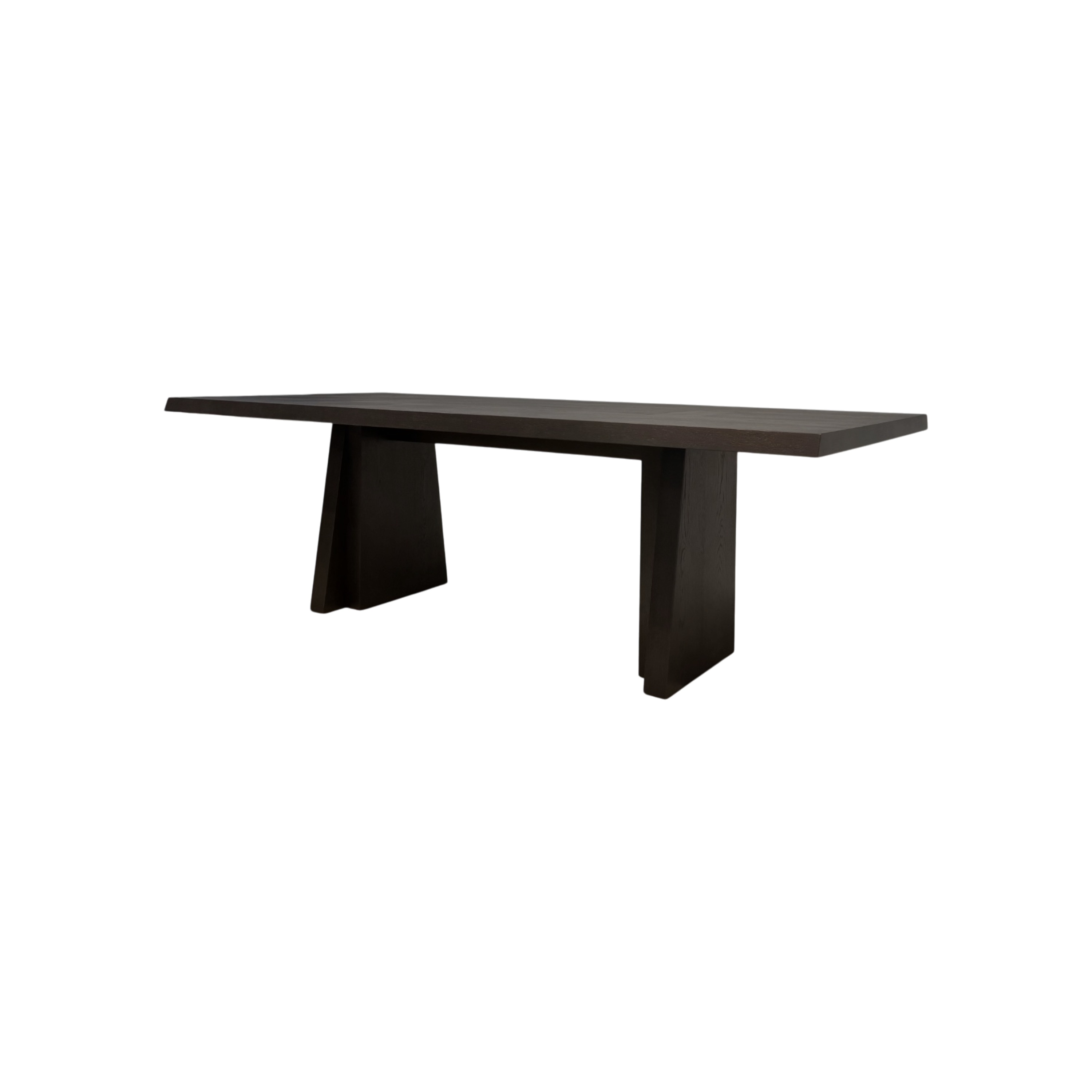Angled view of the Oblique Dining Table showing its elongated dark wood top, chamfered edges and sculptural splayed pedestal bases.
